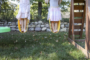 Low section of sisters standing on swings at playground - CAVF52337