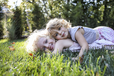 Portrait of sisters lying on grassy field at park - CAVF52340