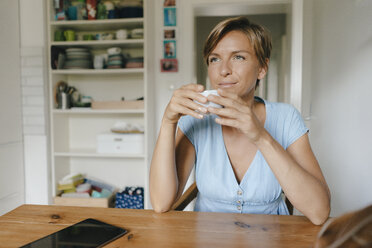Woman sitting at table at home with cup of coffee - KNSF05038