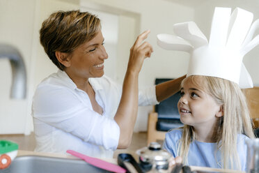Happy mother and daughter playing at home putting on chef's hat - KNSF05039