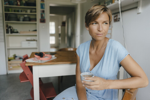 Frau sitzt zu Hause am Tisch mit einer Tasse Kaffee, lizenzfreies Stockfoto