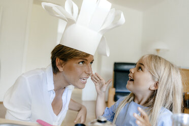 Happy mother and daughter playing at home putting on chef's hat - KNSF05042