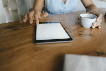 Close-up of woman sitting at table at home with cup of coffee and tablet - KNSF05050