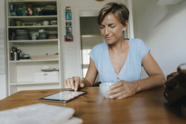 Frau sitzt am Tisch zu Hause mit einer Tasse Kaffee und einem Tablet - KNSF05051