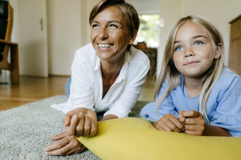 Glückliche Mutter und Tochter, die zu Hause auf dem Boden liegen und etwas anschauen, lizenzfreies Stockfoto