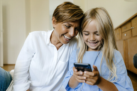 Lachende Mutter und Tochter schauen gemeinsam auf ihr Smartphone, lizenzfreies Stockfoto