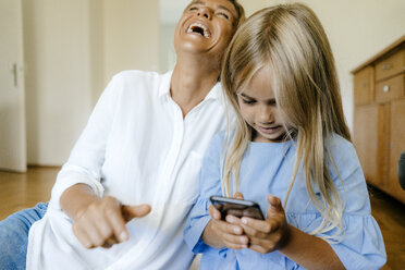 Lachende Mutter und Tochter schauen auf ihr Smartphone - KNSF05060