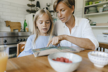 Mother and daughter reading book at table at home together - KNSF05075