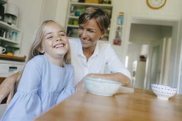 Happy mother and daughter sitting at kitchen table at home - KNSF05079