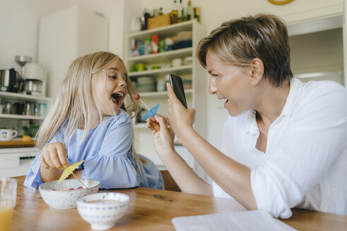 Glückliche Mutter und Tochter, die sich am Tisch zu Hause amüsieren und ein Smartphone-Foto machen - KNSF05084