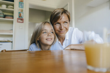 Smiling mother and daughter sitting at kitchen table at home - KNSF05087