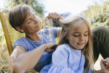 Mother braiding daughter's hair in garden - KNSF05096