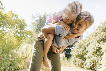 Glückliche Mutter trägt Tochter huckepack im Garten - KNSF05099