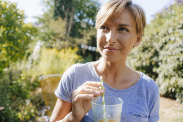 Portrait of woman drinking a soft drink in garden - KNSF05137