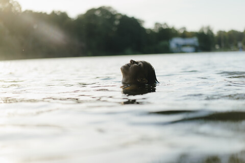 Frau schwimmt in einem See bei Sonnenuntergang, lizenzfreies Stockfoto