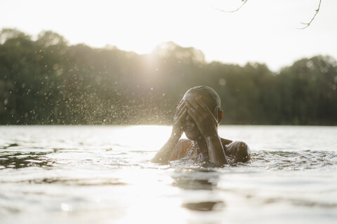 Frau in einem See bei Sonnenuntergang spritzt mit Wasser, lizenzfreies Stockfoto