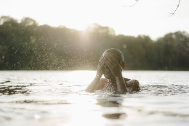 Frau in einem See bei Sonnenuntergang spritzt mit Wasser - KNSF05169