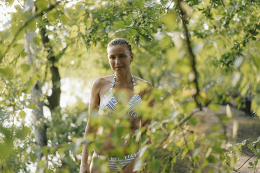 Porträt einer lächelnden Frau im Bikini an einem Baum an einem See - KNSF05173