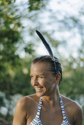 Porträt einer glücklichen Frau mit nassen Haaren, die eine Feder in ihrem Haar trägt - KNSF05177