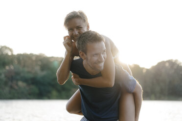 Happy man carrying girlfriend piggyback at a lake - KNSF05183