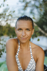 Porträt einer lächelnden Frau mit nassen Haaren, die einen Bikini an einem See trägt - KNSF05189