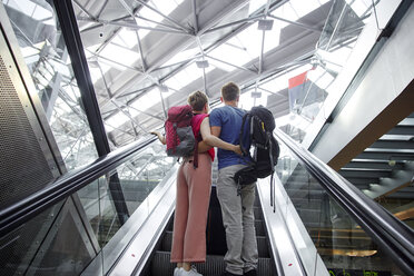 Rückansicht eines Paares auf einer Rolltreppe auf dem Flughafen - RHF02223