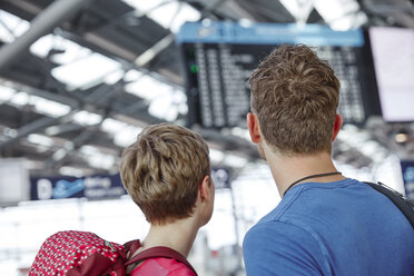 Rear view of couple looking at arrival departure board at the airport - RHF02225