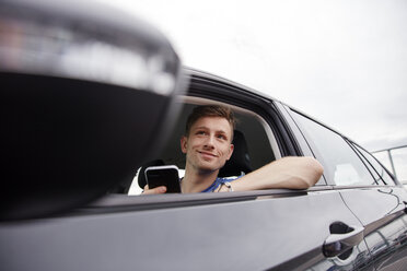 Lächelnder junger Mann mit Mobiltelefon in einem Auto - RHF02263