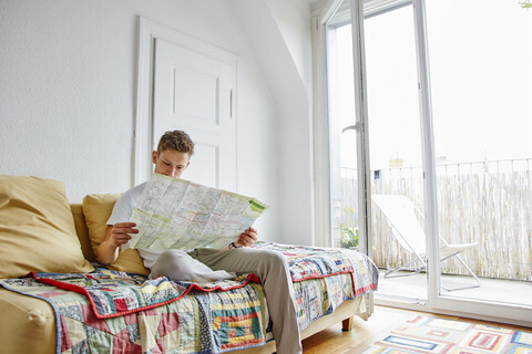 Junger Mann sitzt zu Hause auf der Couch und liest eine Karte, lizenzfreies Stockfoto