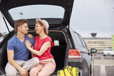 Happy young couple sitting in car boot at the airport - RHF02270