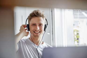Portrait of smiling young man at home listening to music with headphones - RHF02271