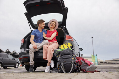 Glückliches junges Paar im Kofferraum eines Autos auf dem Flughafen, lizenzfreies Stockfoto