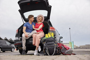 Happy young couple sitting in car boot at the airport - RHF02272