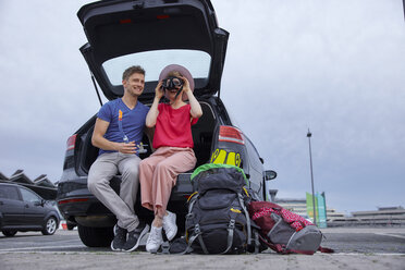 Happy young couple with snorkeling equipment sitting in car boot at the airport - RHF02273