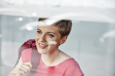 Porträt einer lächelnden Frau mit Rucksack hinter einer Fensterscheibe - RHF02274