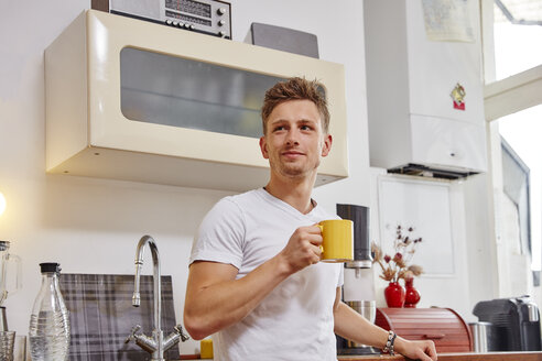 Lächelnder junger Mann zu Hause bei einer Kaffeepause in der Küche - RHF02279