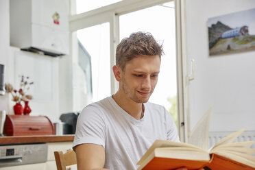 Lächelnder junger Mann, der zu Hause ein Buch liest - RHF02281