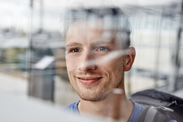 Porträt eines lächelnden jungen Mannes, der aus dem Fenster schaut - RHF02282