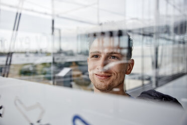 Porträt eines lächelnden jungen Mannes auf dem Flughafen, der aus dem Fenster schaut - RHF02284