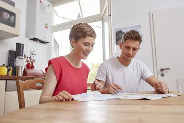 Smiling young couple sitting at table at home with map - RHF02286