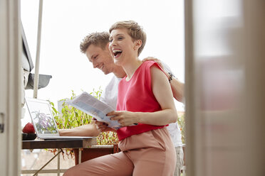 Happy couple on balcony at home with laptop and map - RHF02293