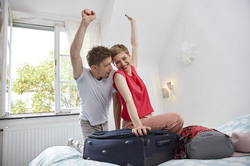 Glückliches Paar mit Koffer für den Sommerurlaub auf dem Bett - RHF02312