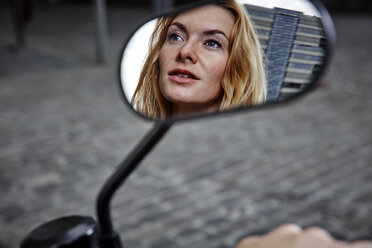 Porträt einer selbstbewussten jungen Frau, die sich im Außenspiegel eines Motorrads spiegelt - RHF02313