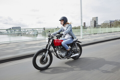 Germany, Cologne, young woman riding motorcycle on bridge stock photo