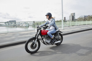 Deutschland, Köln, junge Frau fährt Motorrad auf Brücke - RHF02321