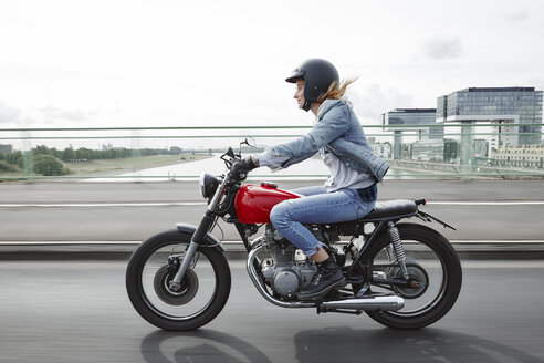 Deutschland, Köln, junge Frau fährt Motorrad auf Brücke - RHF02326