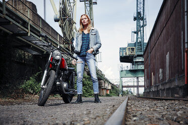 Portrait of confident young woman standing next to motorcycle - RHF02344