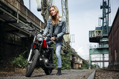 Porträt einer selbstbewussten jungen Frau, die auf ein Motorrad steigt, lizenzfreies Stockfoto