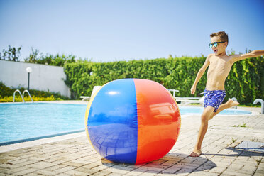Junge am Pool Sonnenbrille kicking großen Strand Ball - DIKF00300
