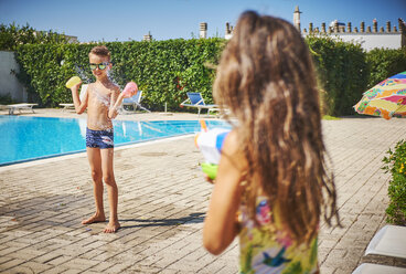 Mädchen mit Wasserpistole spritzt auf Junge mit Wasserbomben am Pool - DIKF00310